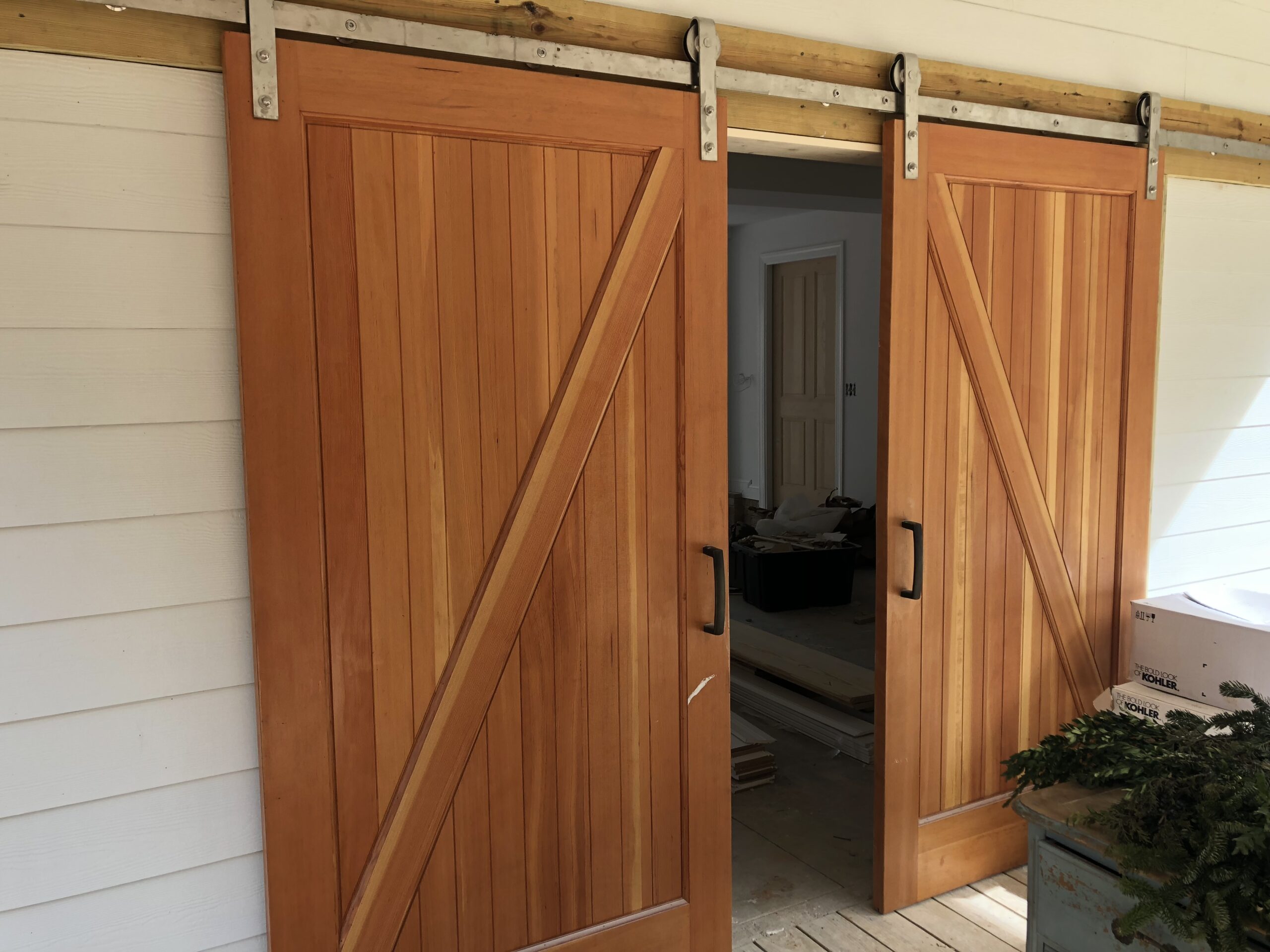 A pair of wooden sliding barn doors with Z-braces are partially open, revealing a room with a light-colored door inside.