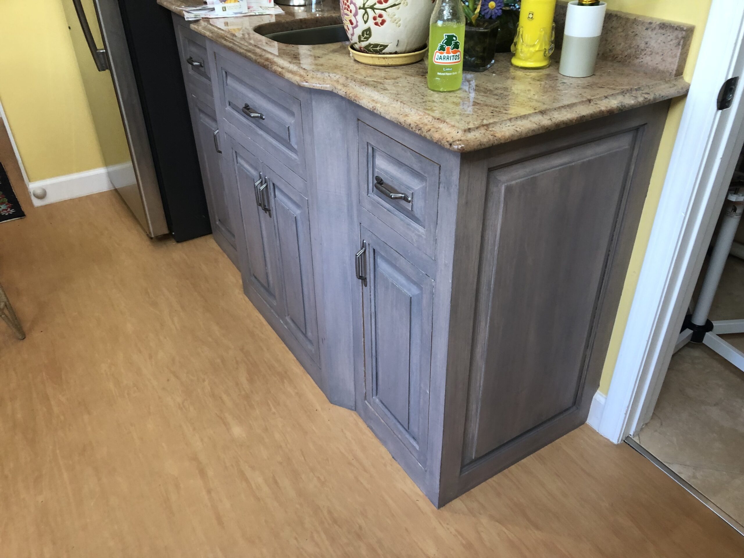 A wooden kitchen cabinet with a granite countertop, featuring drawers and doors, is set against a wall.